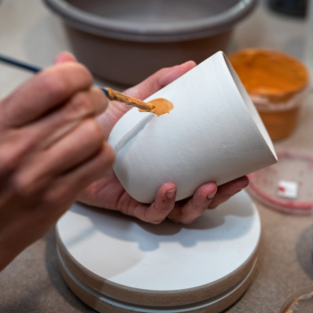 Deltager maler og dekorerer kopper på keramik workshop for firmaer og private.