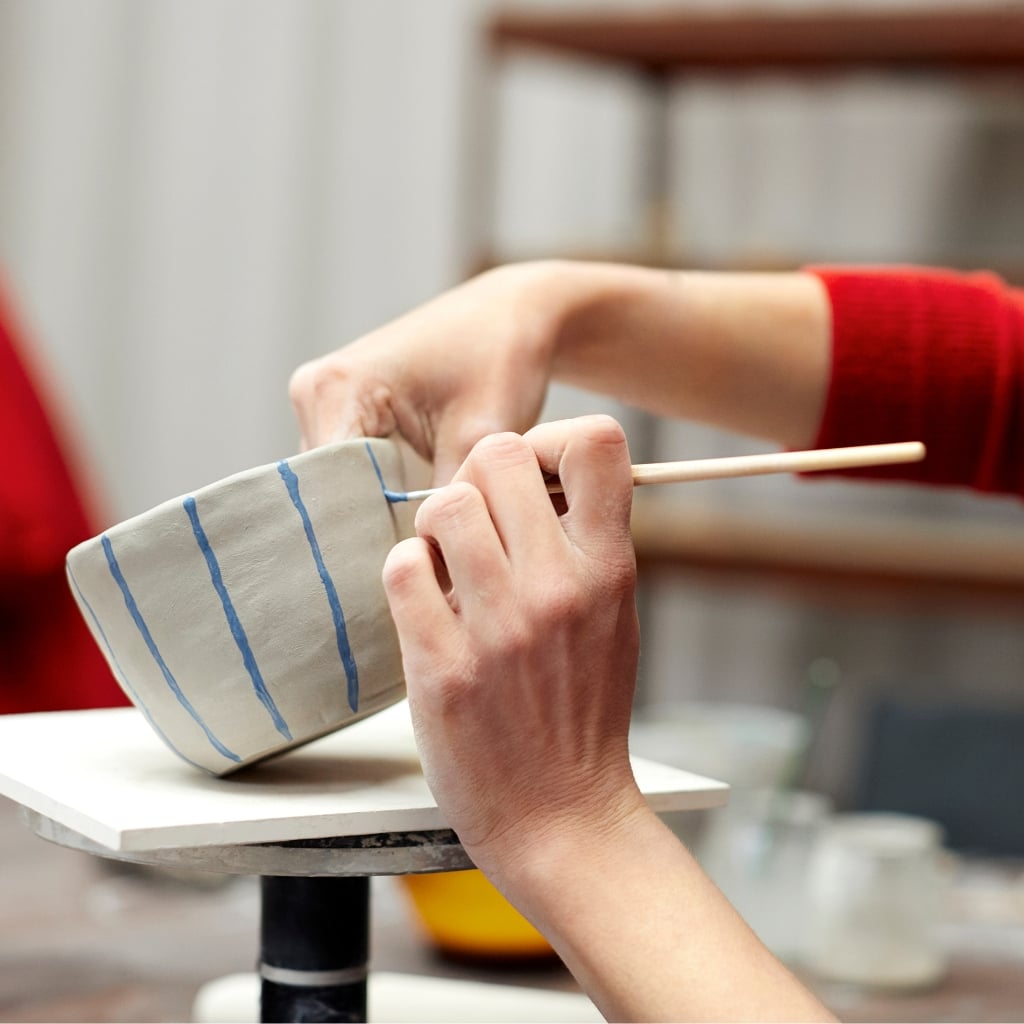 Kursist maler striber på en kop til en kreativ keramik workshop, polterabend, firmafest eller teambuilding.