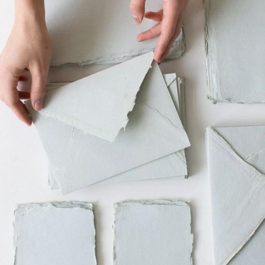 Billedet viser håndlavet papir der er foldet som konvolutter, de er lavet af bæredygtige genbrugsmaterialer på en kreativ workshop. 